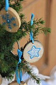 Small slices of tree trunk painted with blue and white star motifs hung from fir branches with blue ribbon
