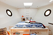 Custom bed on platform with porthole windows on either side in houseboat