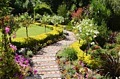 Garden path made from old railway sleepers lined with flowerbeds, low hedges and standard roses