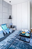 Breakfast tray on double bed with scatter cushions and blanket in shades of blue in bedroom with fitted wardrobes