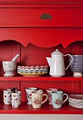 Plates and mugs on red-painted, country-house-style dresser