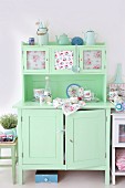 Pale green, vintage kitchen dresser romantically decorated with pastel enamel crockery, rose-patterned china and floral fabrics