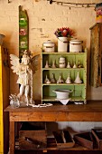 Angel figurine and small shelving unit painted green holding collection of funnels on wooden table