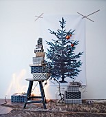 Stacked gifts wrapped in black and white paper below Christmas tree print on wall