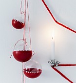 Glass baubles partly dipped in red paint and decorated with pattern of crosses next to lit candle