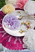 Romantic flowers made from folded serviettes on floral plate with silver cutlery
