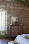 Two table lamps and mirror on top of antique chest of drawers in Mediterranean bedroom with stone walls