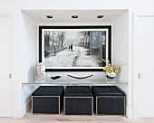 Large black and white picture in niche above glass shelf and black pouffes