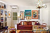 Colourful living room in artist's apartment with comfortable, red leather sofa, various pictures and frames