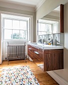 Wooden washstand, patterned rug on wooden floor and deep-set window in background