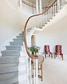 Curved staircase with pale grey runner and chairs with patterned upholstery in elegant foyer