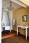 Vintage-style bathroom with yellow walls, wooden floor, washstand and free-standing bathtub on platform