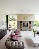 Grey Chesterfield sofa and marble coffee table in front of modern fireplace with firewood niches