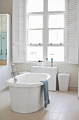 Freestanding bathtub in bright bathroom with shutters