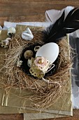 Vintage-style Easter arrangement of duck's egg on cake tin in straw next with quail's eggs and black feather
