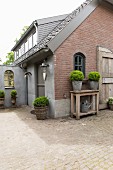 Planters on wooden table against brick gable-end wall and paved courtyard outside house with dormer windows