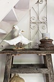 Stuffed geese and candle in wooden candle holder on rustic wooden table below staircase
