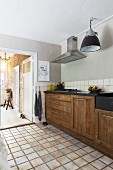 Solid wooden base units and dark stone worksurface in rustic kitchen with pale terracotta floor and open door in background