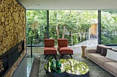 Designer sofa, chaise armchairs and mirrored coffee table in front of fireplace in wall decorated with slices of tree trunk