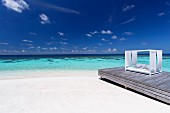 Sofa with awning on wooden jetty on sandy beach (Maldives)