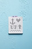 DIY cross-stitch pattern on graph paper stuck on sky-blue wall with washi tape