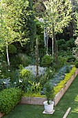 Von Natursteinplatten eingefasste Pflanzbeete und Bäume im Garten