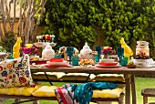 Colourful, set table with lanterns, animal figurines, yellow seat cushions on bench and ethnic scatter cushions