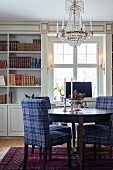 Tartan upholstered chairs at round table below antique chandelier in front of bookcases