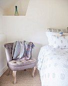 Antique, rustic-style easy chair next to bed below delicate vase in corner niche