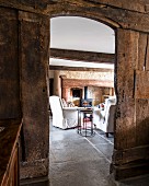 Open doorway in rustic board wall leading to comfortable white armchairs in front of fireplace