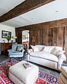 Pale ottoman, couch and armchair against rough board wall in rustic living room