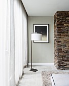 Modern standard lamp with white lampshade in corner next to floor-length curtain