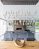 Pendant lamp with suspended glass droplets above dining table in front of grey sofa and fireplace in lounge area