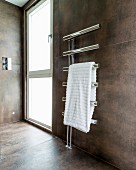White towel on heated chrome towel rail in modern bathroom with large tiles