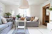 Ländliches Wohnzimmer mit Polstercouch und weiss lackiertem Beistelltisch unter Pendelleuchte mit weißem Stoffschirm