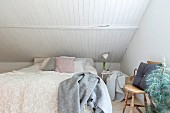 Lace bedspread on double bed below sloping ceiling with white wood cladding