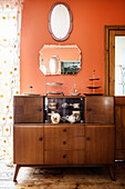 Old wooden sideboard below vintage mirrors on orange wall