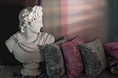 Bust of the god Apollo next to grey and pink velvet cushions on antique table