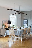 Festively set Christmas dining table with Scandinavian cane chairs and lights suspended from branch