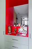 Fitted cabinets painted pale grey with mirror on back wall of red niche