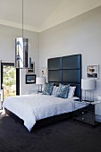 Double bed with tall, black-upholstered headboard and cylindrical pendant lamp in elegant bedroom