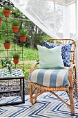 Scatter cushions on wicker chair with upholstered seat next to pots of lavender hung on rebar grille in garden pavilion