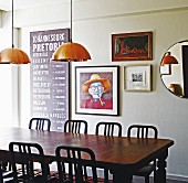 Traditional dining table and chairs made from dark wood below copper pendant lamps in front of framed pictures