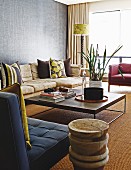 Sofa and armchairs around modern coffee table on sisal carpet with turned wooden side table in foreground