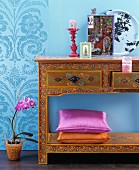 Deko-Accessoires auf reichverziertem Wandkonsolentisch mit floralen Mustern vor blauer Wand
