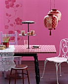 Mixture of styles in pink colour scheme: cake stand on dining table, various chairs and Oriental paper lanterns