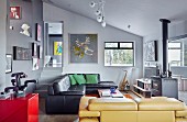 Black leather couch and yellow leather couch in open-plan, artistic interior with grey walls and gallery of pictures