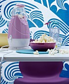 Iconic purple popcorn machine on dining table in front of fabric with blue and white pattern of waves