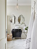 Modern countertop sink on black antique chest of drawers below two mirrors with floral forms seen through open country-house door