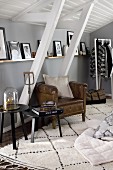 Leather armchair and side tables under pictures on narrow shelf and sloping ceiling